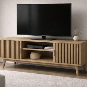 Op de afbeelding: Een lichtbruine houten tv-standaard met een grote zwarte televisie erbovenop. De standaard heeft een lamellendeurontwerp en bevat open schappen voor media-componenten en een geweven mand. De standaard is 152 cm breed.