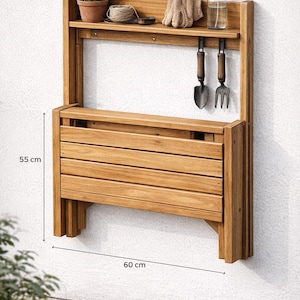 May include: A wooden potting bench, 21.65 inches high and 23.62 inches wide, with a shelf, tools, and a small plant. Includes a folding work surface. The bench is made of light brown wood and is mounted on a white wall.