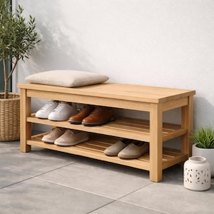 May include: A light oak shoe storage bench with two slatted shelves and a padded top. A beige cushion rests on the bench. Several pairs of shoes are arranged on the shelves. A potted plant is nearby.