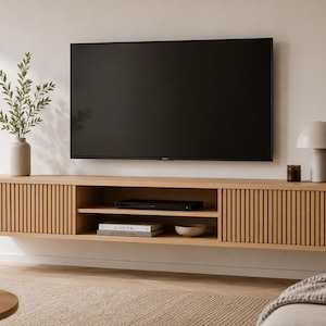 May include: A light oak floating media unit with a slatted door design, mounted below a large black television. The unit has open shelving and is complemented by a decorative lamp and vase.