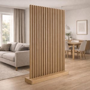 Puede incluir: Un separador de ambientes de madera con lamas verticales, sobre una base rectangular. El separador es de color marrón claro y está situado en un salón con un sofá, una mesa de centro y una alfombra.