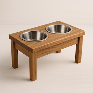 May include: A wooden pet feeder with two stainless steel bowls. The feeder is made of light brown wood and has a rectangular top with two circular cutouts for the bowls. The feeder is elevated on four square legs.