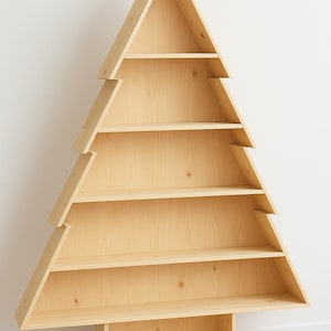 Könnte beinhalten: Ein Bücherregal aus Holz in Form eines Weihnachtsbaums. Die Regale in Naturholzoptik sind in einer dreieckigen Form mit mehreren horizontalen Regalen angeordnet. Das Bücherregal steht auf einem rechteckigen Sockel und vor einer weißen Wand.