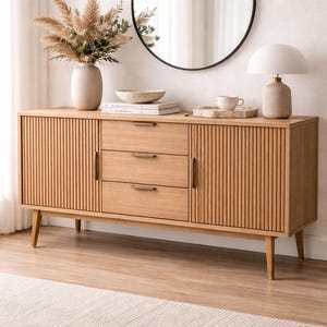 Può includere: Credenza in legno chiaro con tre cassetti e due ante, con dettagli scanalati verticali. Uno specchio rotondo con cornice nera è appeso sopra, con un vaso di fiori secchi e una lampada. Un tappeto neutro è in primo piano.