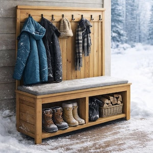 May include: Wooden entryway bench with a gray cushion, storage shelf, and coat rack. The bench holds boots and a basket of firewood. Coats, a hat, and a scarf hang on the rack. The scene is set outdoors in a snowy environment.
