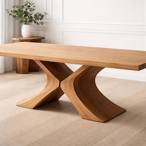 Op de afbeelding: Een rechthoekige eettafel van lichtbruin hout met een uniek onderstel. De tafel heeft een glad oppervlak en een lichte afwerking. De basis heeft een gebogen, kruisend ontwerp. De tafel staat in een goed verlichte kamer.