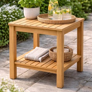 Könnte beinhalten: Heller Beistelltisch aus Holz mit Lattenrost und unterem Regal. Auf der Oberseite befindet sich ein geflochtener Tablett mit Gläsern und einer Wasserkaraffe. Ein Blumentopf, ein gefaltetes Handtuch und ein Korb sind ebenfalls sichtbar.