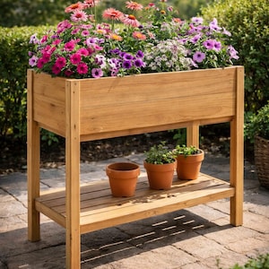 Op de afbeelding: Een verhoogde houten plantenbak gevuld met levendige roze, paarse en witte bloemen. De plantenbak heeft een onderste plank met drie terracotta potten. De structuur is gemaakt van lichtgekleurd hout en staat op een stenen terras.