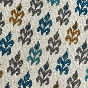 May include: A white fabric with a repeating pattern of stylized floral motifs in shades of teal, gray, and gold.