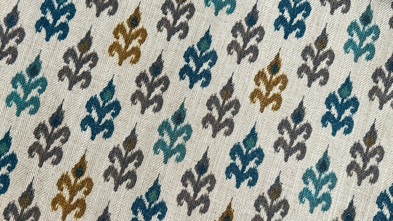 May include: A white fabric with a repeating pattern of stylized floral motifs in shades of teal, gray, and gold.