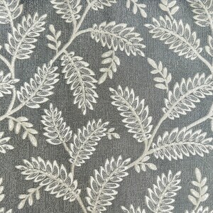 K&ouml;nnte beinhalten: Nahaufnahme eines grauen Stoffes mit einem wei&szlig;en Blumenmuster. Das Muster zeigt zarte, stilisierte Bl&auml;tter und Zweige.