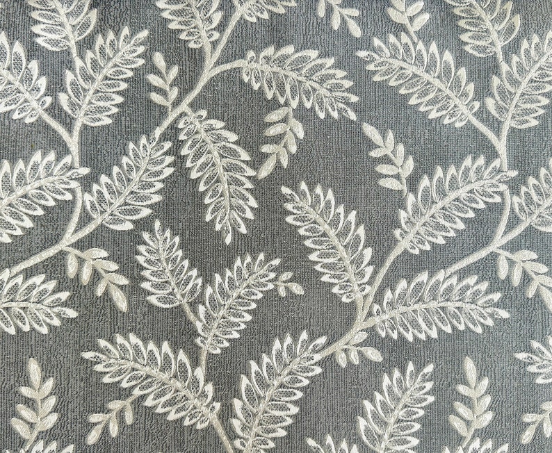 K&ouml;nnte beinhalten: Nahaufnahme eines grauen Stoffes mit einem wei&szlig;en Blumenmuster. Das Muster zeigt zarte, stilisierte Bl&auml;tter und Zweige.