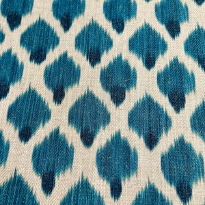 May include: A close-up of a fabric with a blue and white ikat pattern. The fabric has a textured surface and a repeating pattern of blue teardrop shapes on a white background.