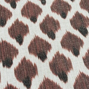 May include: A close-up of a white fabric with a brown and black animal print pattern. The fabric has a subtle herringbone weave.