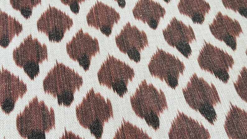 May include: A close-up of a white fabric with a brown and black animal print pattern. The fabric has a subtle herringbone weave.