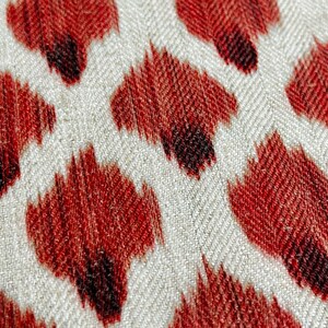 May include: Close-up of a fabric with a red and white chevron pattern. The fabric has a textured surface and is decorated with a repeating pattern of red and black abstract shapes.