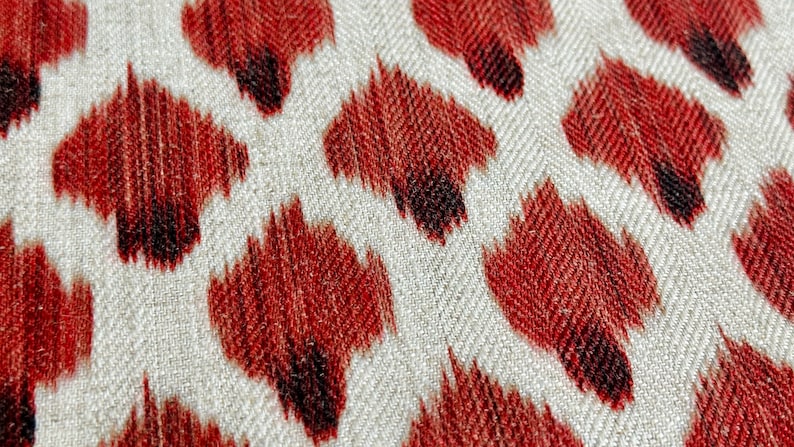May include: Close-up of a fabric with a red and white chevron pattern. The fabric has a textured surface and is decorated with a repeating pattern of red and black abstract shapes.