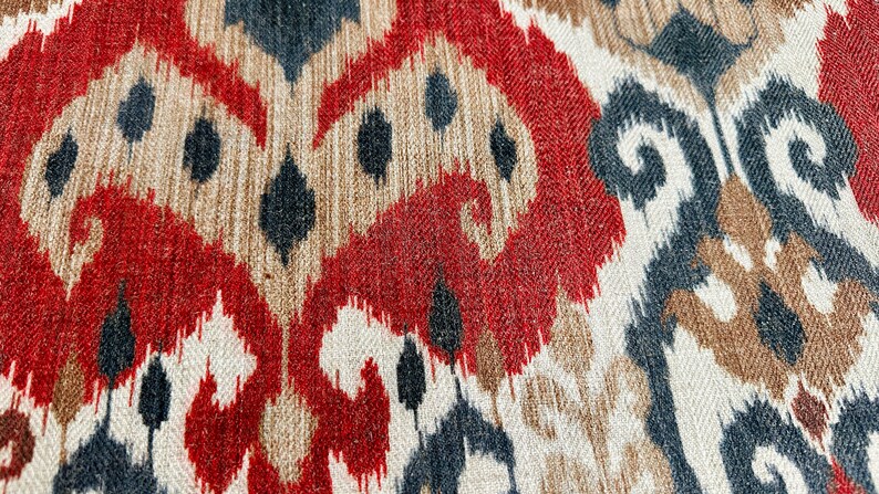 May include: Close-up of a fabric with a red, brown, black and white ikat pattern.