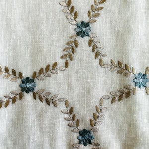 Puede incluir: Tela blanca con un patr&oacute;n repetido de hojas marrones y flores azules bordadas.