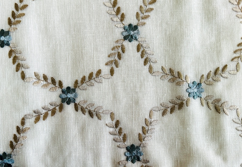 Puede incluir: Tela blanca con un patr&oacute;n repetido de hojas marrones y flores azules bordadas.