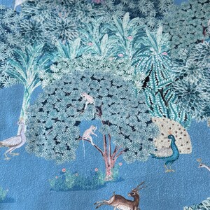 May include: A blue fabric with a printed design of a jungle scene. The scene includes a peacock, a deer, monkeys, and birds. The fabric has a light blue background with green and white foliage.