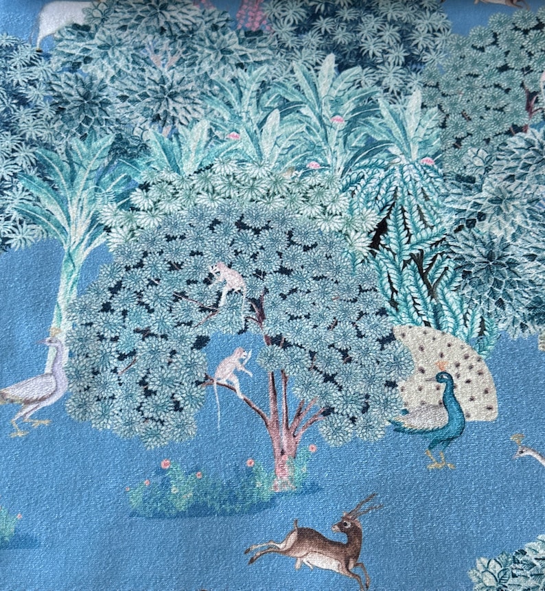 May include: A blue fabric with a printed design of a jungle scene. The scene includes a peacock, a deer, monkeys, and birds. The fabric has a light blue background with green and white foliage.
