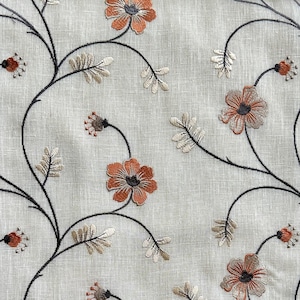 K&ouml;nnte beinhalten: Ein beigefarbener Stoff mit gestickten Blumendesigns in Schwarz und Orange. Die Blumen sind stilisiert und haben ein einfaches Design.