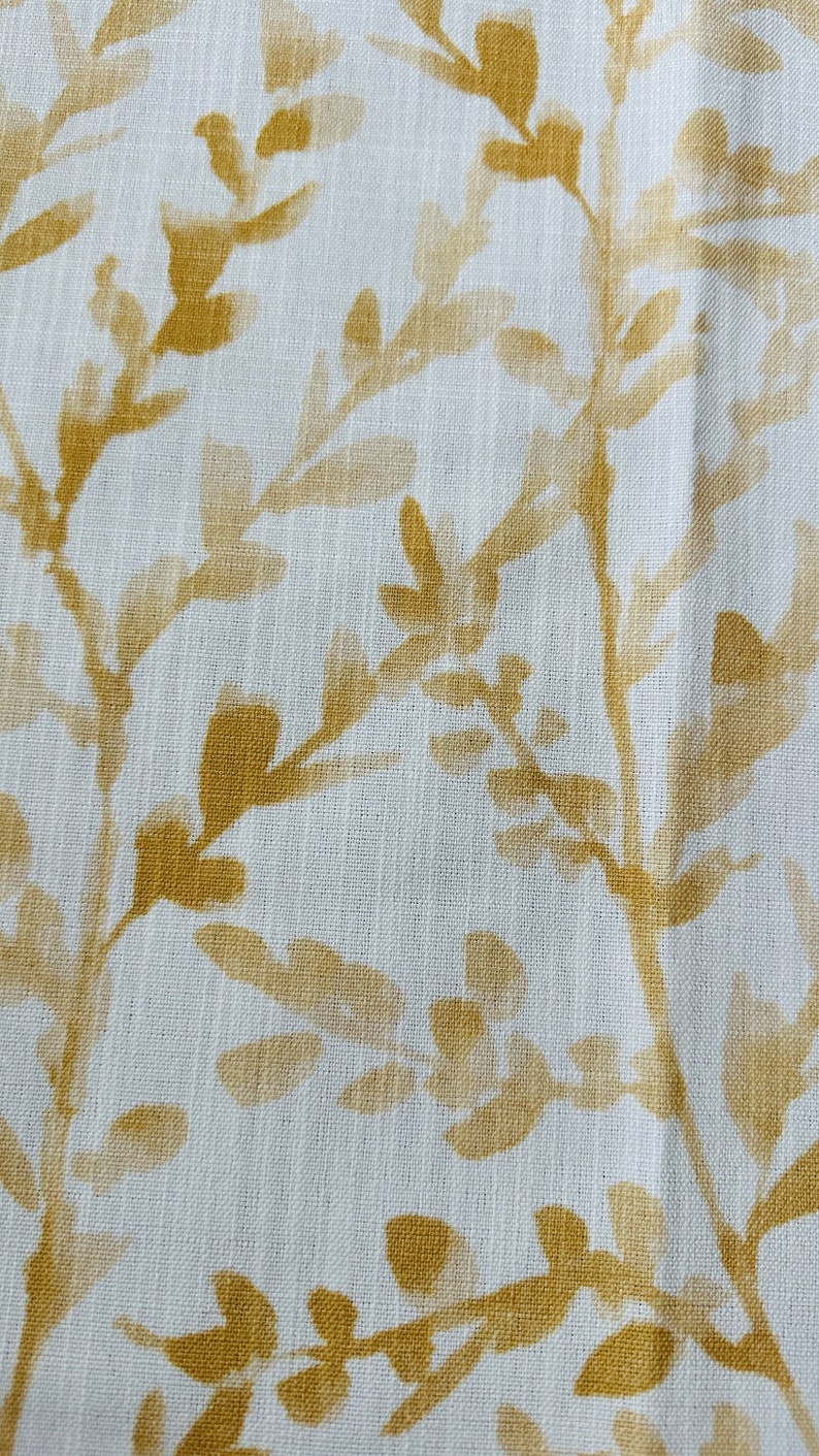 May include: White fabric with a subtle texture featuring a repeating pattern of gold leaf branches. The branches are stylized and have a faded, watercolor-like appearance.
