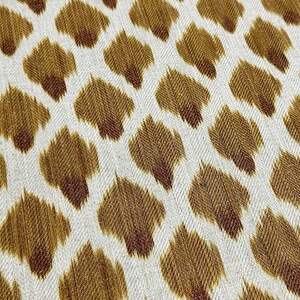 May include: White fabric with a brown ikat pattern. The pattern is a repeating design of small, teardrop-shaped figures.