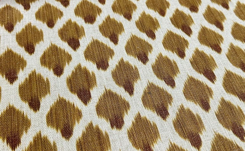 May include: White fabric with a brown ikat pattern. The pattern is a repeating design of small, teardrop-shaped figures.