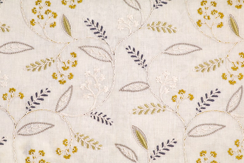 May include: White fabric with an embroidered floral pattern in shades of gray, yellow, and white. The design features delicate leaves and small flower clusters.