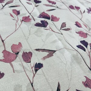 May include: A white fabric with a subtle texture featuring a repeating pattern of dark purple and pink watercolor floral sprigs.