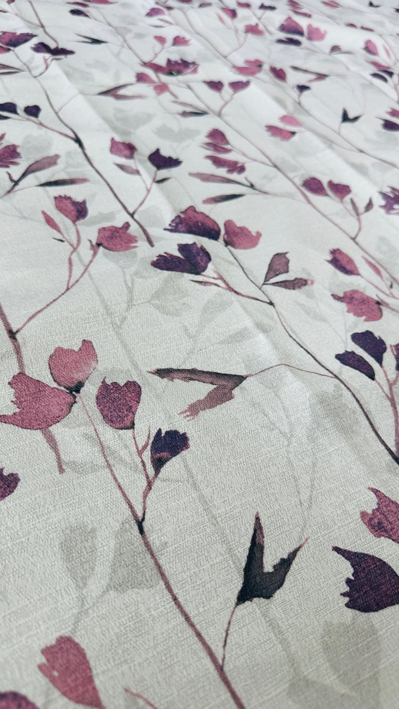 May include: A white fabric with a subtle texture featuring a repeating pattern of dark purple and pink watercolor floral sprigs.