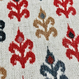 May include: A close-up of a fabric with a repeating pattern of stylized floral motifs in red, black, and brown on a white background.