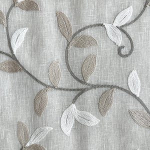 May include: A close-up of a beige fabric with embroidered brown and white leaves. The leaves are arranged in a pattern of vines.