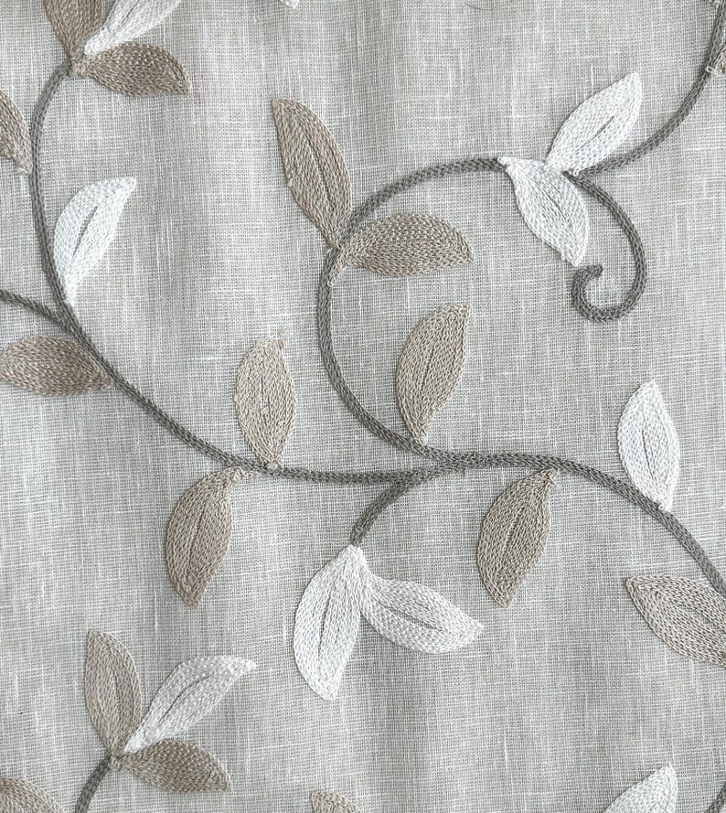 May include: A close-up of a beige fabric with embroidered brown and white leaves. The leaves are arranged in a pattern of vines.