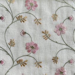 Puede incluir: Tela blanca con flores rosas y hojas doradas bordadas. El patr&oacute;n floral se repite en toda la tela.