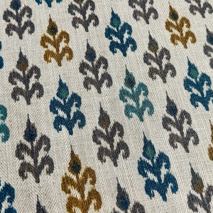 May include: A white fabric with a repeating pattern of stylized floral motifs in shades of teal, brown, and gold.