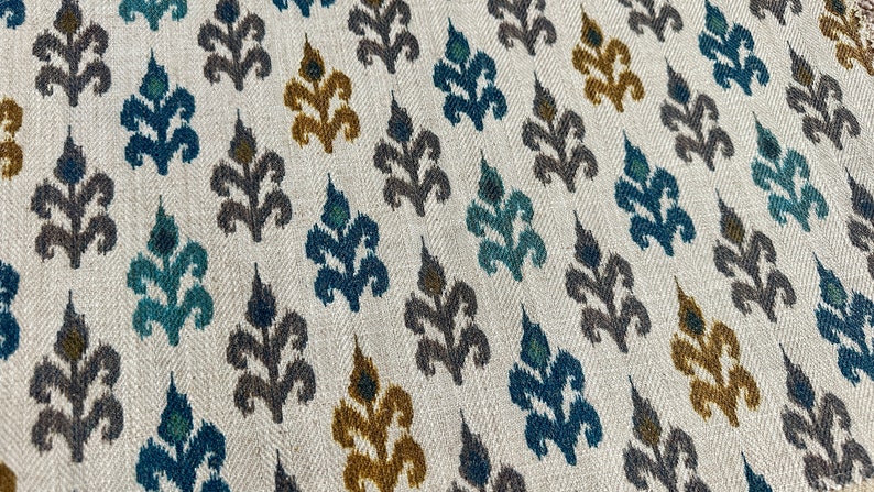 May include: A white fabric with a repeating pattern of stylized floral motifs in shades of teal, brown, and gold.