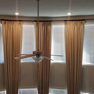 May include: A high-angle view of a room with beige curtains and blinds. The curtains are draped on a curved rod above the windows. A ceiling fan hangs in the center, and two recessed lights are visible.