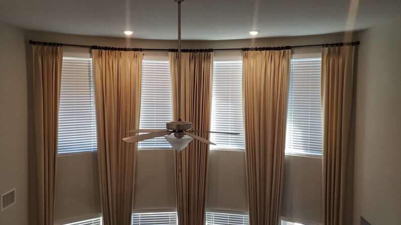 May include: A high-angle view of a room with beige curtains and blinds. The curtains are draped on a curved rod above the windows. A ceiling fan hangs in the center, and two recessed lights are visible.