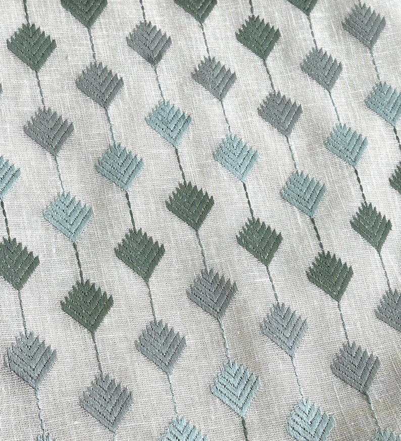 May include: A white fabric with a repeating pattern of green and blue diamond shapes. The diamonds are made of a textured fabric and are arranged in a diagonal pattern.