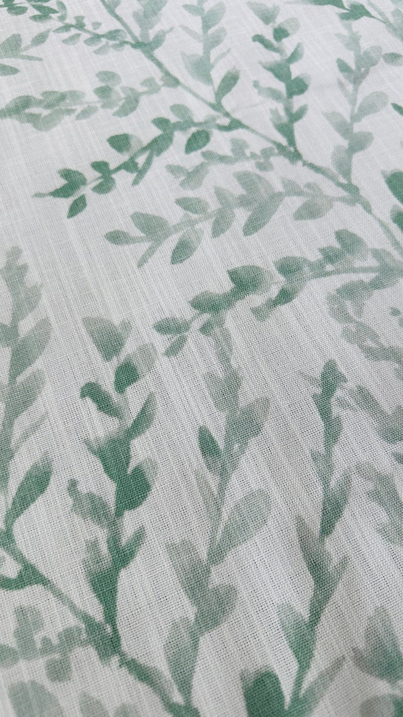 May include: White fabric with a green leafy pattern. The leaves are a muted green color and are printed on a white background.