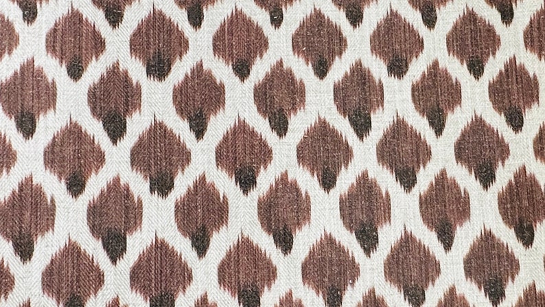 May include: A white fabric with a brown and black ikat pattern. The pattern is a repeating design of small, teardrop-shaped figures.
