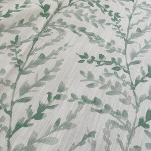 May include: A white fabric with a green leafy pattern. The leaves are a watercolor style and are scattered across the fabric.