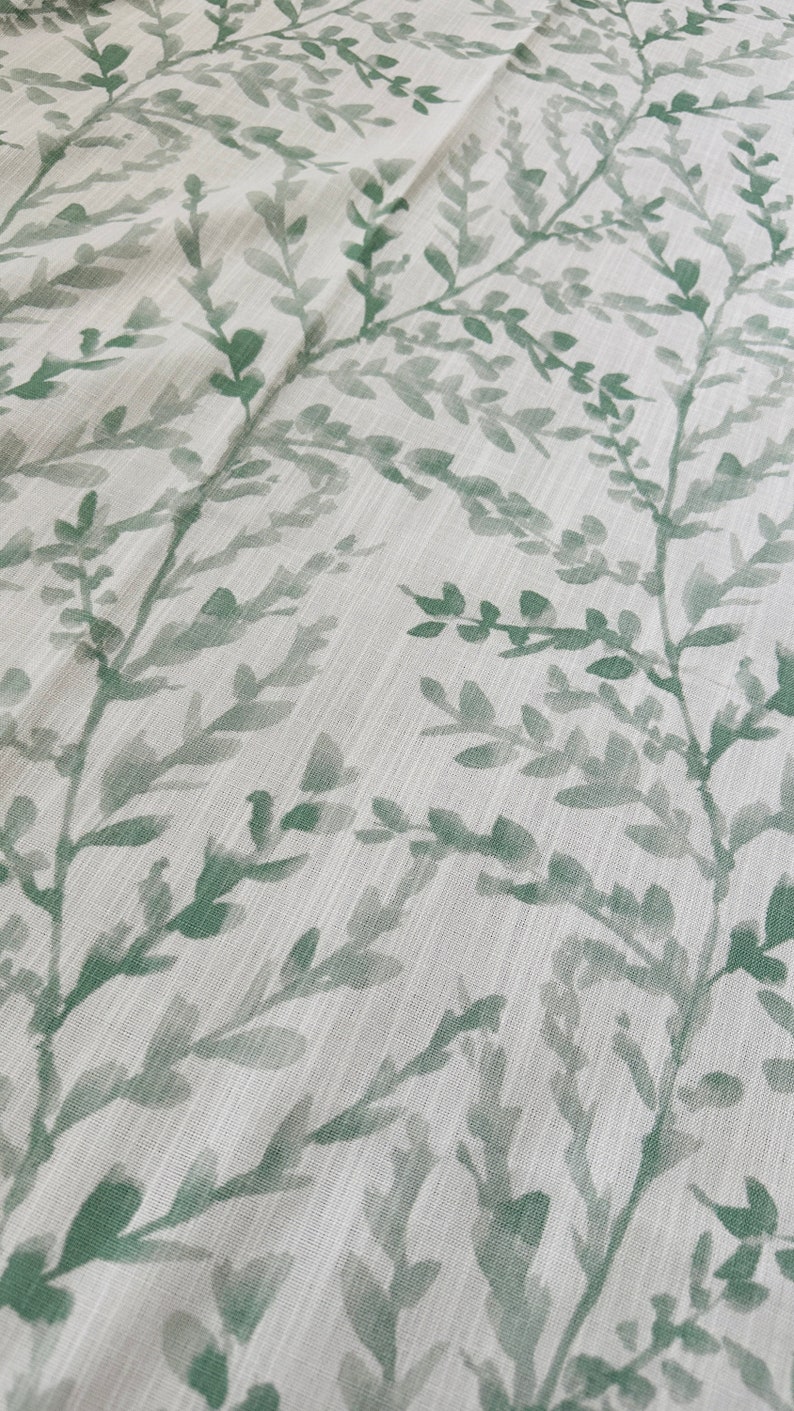 May include: A white fabric with a green leafy pattern. The leaves are a watercolor style and are scattered across the fabric.