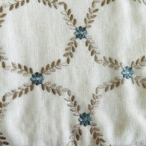 Puede incluir: Una tela blanca con un delicado patr&oacute;n bordado de hojas marrones y flores azules. El dise&ntilde;o se repite en toda la tela, creando un aspecto sutil y elegante.