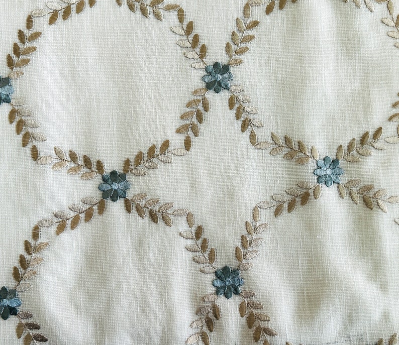 Puede incluir: Una tela blanca con un delicado patr&oacute;n bordado de hojas marrones y flores azules. El dise&ntilde;o se repite en toda la tela, creando un aspecto sutil y elegante.