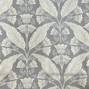 Pu&ograve; includere: Un tessuto grigio con un motivo floreale bianco. Il motivo presenta foglie e fiori stilizzati con un aspetto testurizzato, quasi metallico.