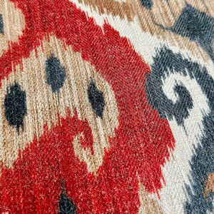 May include: Close-up of a fabric with a red, white and black ikat pattern. The fabric has a textured, woven appearance.